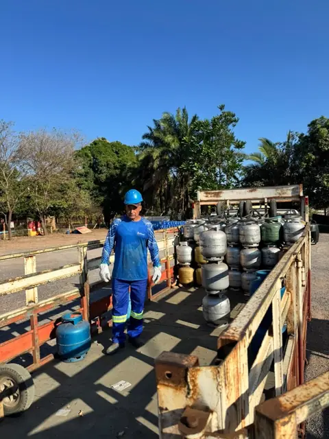 Colaborador da Pantanal Gás de uniforme e capacete sobre a carroceria de um caminhão com botijões