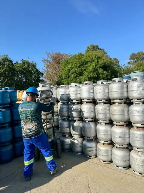 Colaborador de capacete movimentando botijões com carrinho entre as pilhas do estoque